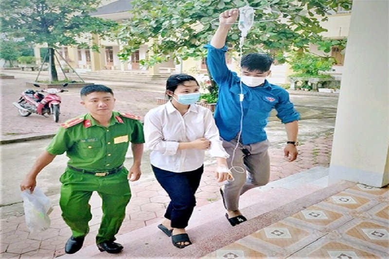 Nhung (áo trắng) được tình nguyện viên và công an hỗ trợ đưa vào phòng thi khi tay trái đang truyền dịch, sáng 7/7. (Ảnh: Hùng Lê).