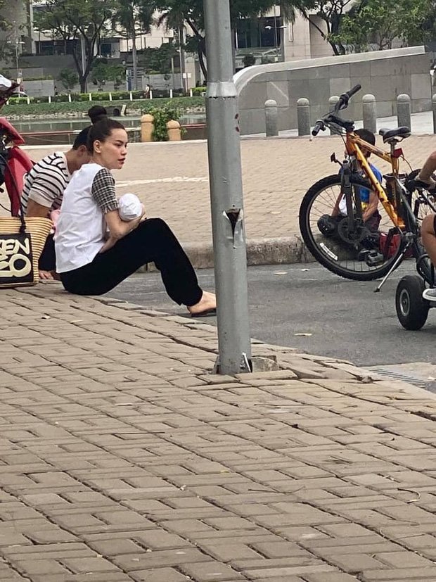 Hồ Ngọc Hà và Kim Lý ngồi bệt tại vỉa hè vừa bế con vừa nhìn Subeo chơi phía xa