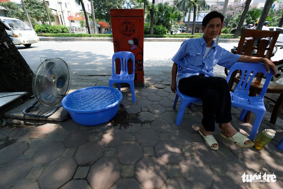 Một nhân viên bảo vệ trên đường Hoàng Quốc Việt, Hà Nội đặt chậu nước lớn trước quạt để bớt cái hấp nóng từ mặt đường - Ảnh: NAM TRẦN