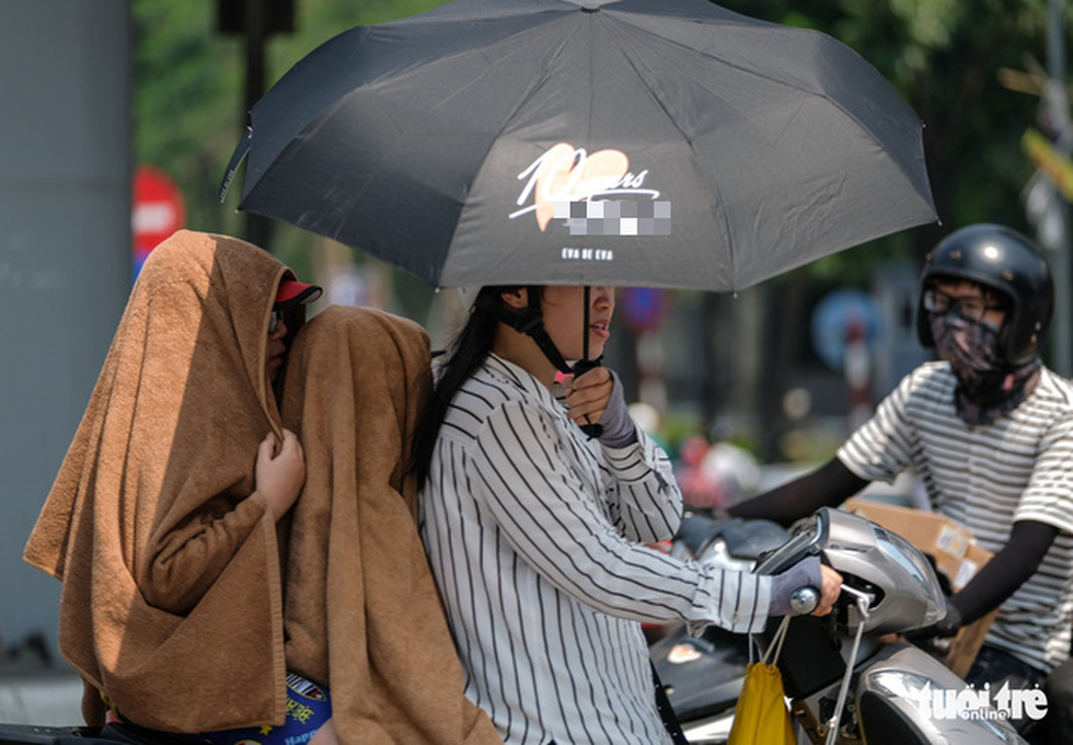 Hai em nhỏ cùng mẹ được trùm kín khăn, che ô trên đường Láng Hạ, Hà Nội - Ảnh: NAM TRẦN