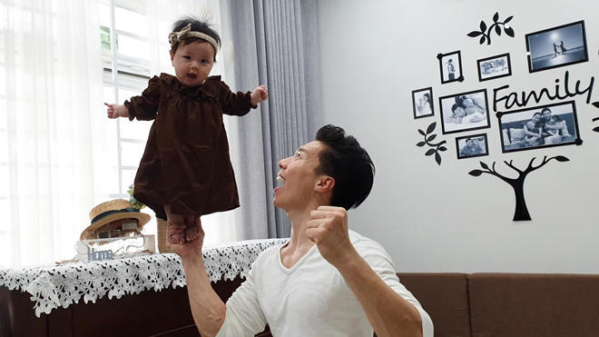Quốc Nghiệp nâng con gái 8 tháng tuổi bằng một tay. 