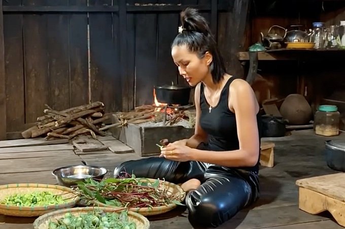 Hoa hậu H'Hen ngồi bệt dưới sàn nhà, ăn mặc giản dị nấu những món truyền thống Êđê.