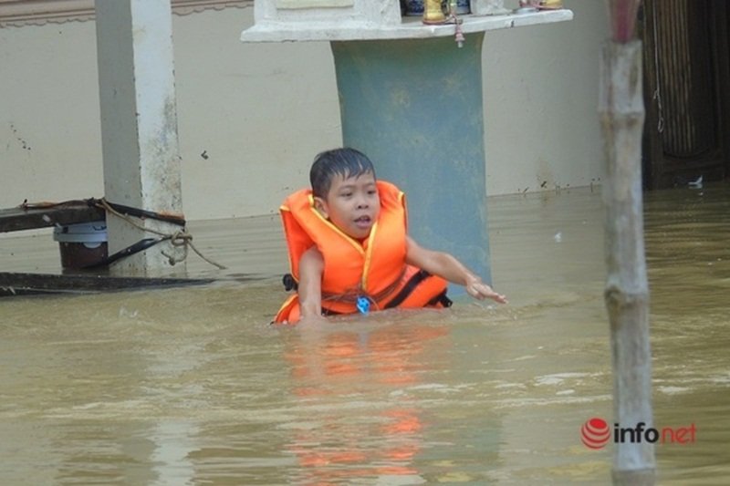 Cháu bé mặc áo phao bơi trong nước lũ. (Ảnh: Infonet).