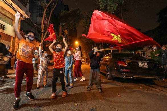 Nhiều em nhỏ đeo khẩu trang reo hò cùng lá cờ tổ quốc. Ảnh: Tuổi trẻ.