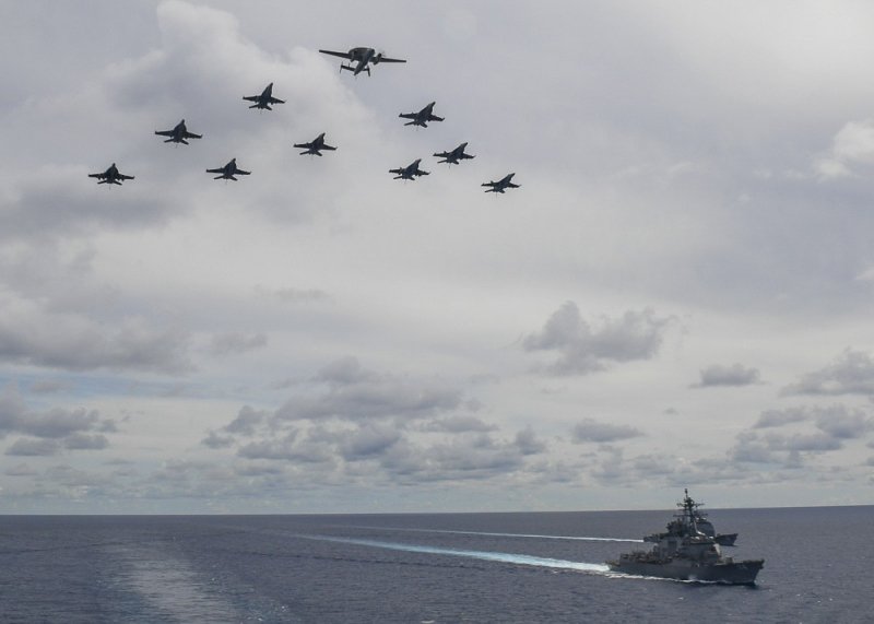 Máy bay chỉ huy và cảnh báo sớm trên không E-2C Hawkeyes dẫn đầu đội hình tiêm kích F/A-18 E/F Super Hornet bay phía trên 2 tàu hộ tống cho tàu sân bay